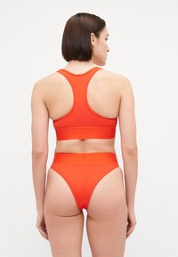Röd sport-bh och höga bikiniunderdelar tillverkade av mjukt, sträckt material. Har racerback-design och bred midja.