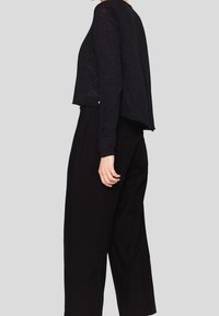 Svart långärmad topp med lös passform, tillverkad av lättviktig tyg; kombinerad med vida svarta byxor, vilket skapar en monokrom look.