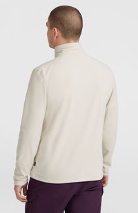 Pullover in pile crema con collo alto e maniche lunghe, caratterizzato da una texture liscia e un piccolo etichetta all'orlo.
