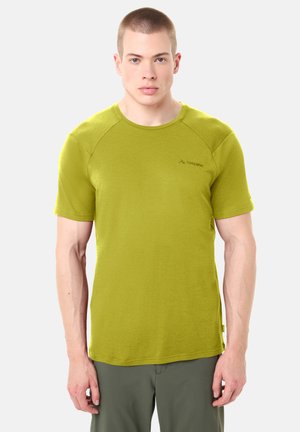 Giovane uomo in piedi di fronte, indossa una maglietta verde lime a maniche corte e pantaloni grigi su uno sfondo semplice e chiaro.