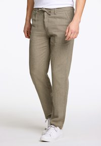 Helle beige, gewebte Stoffhose mit lockerer Passform, Kordelzugbund und seitlichen Taschen. Kombiniert mit weißen Sportschuhen.