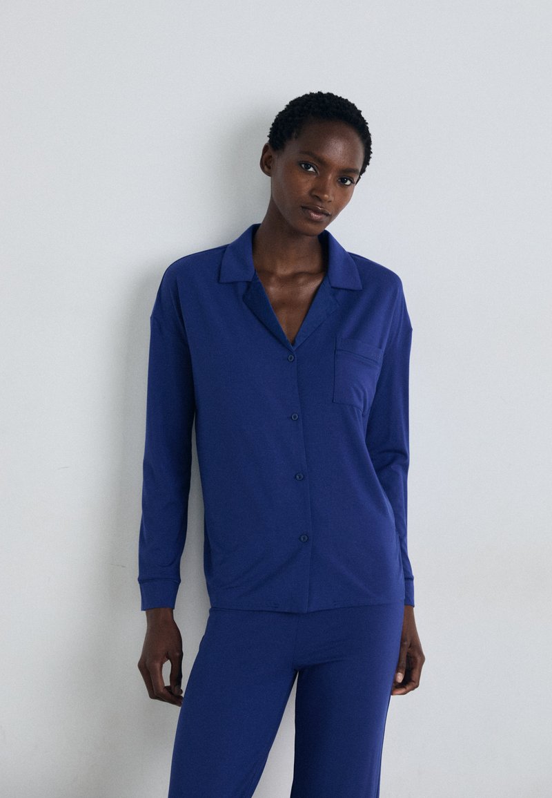 Ensemble de pyjama bleu marine avec un haut à manches longues à boutons comportant une poche et un pantalon assorti, fabriqué dans un tissu lisse et doux.