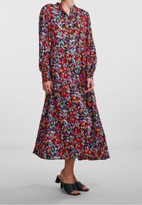 Pitkähihainen, nappikiinnitteinen mekko, jossa on eloisa kukkakuvio punaisilla, vaaleanpunaisilla ja sinisillä terälehdillä tummalla pohjalla. Liehuva siluetti.