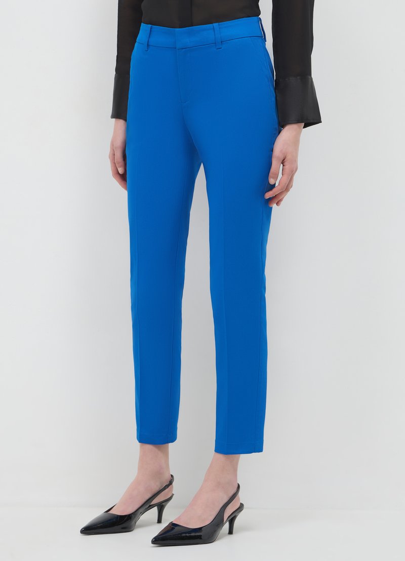 Pantaloni blu cropped e aderenti in tessuto liscio, con cintura piatta e tasche laterali. Abbinati a décolleté slingback nere in vernice.