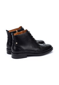 Bottes noires en cuir, à la cheville, avec des détails brogue, bout rond et petit talon empilé. Intérieur doublé en cuir tan. Fermeture à lacets à l'avant.