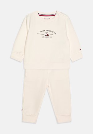 Completo sportivo a due pezzi color crema realizzato in tessuto morbido, composto da un top a maniche lunghe con stampa del logo e pantaloni jogger abbinati con polsini a costine.