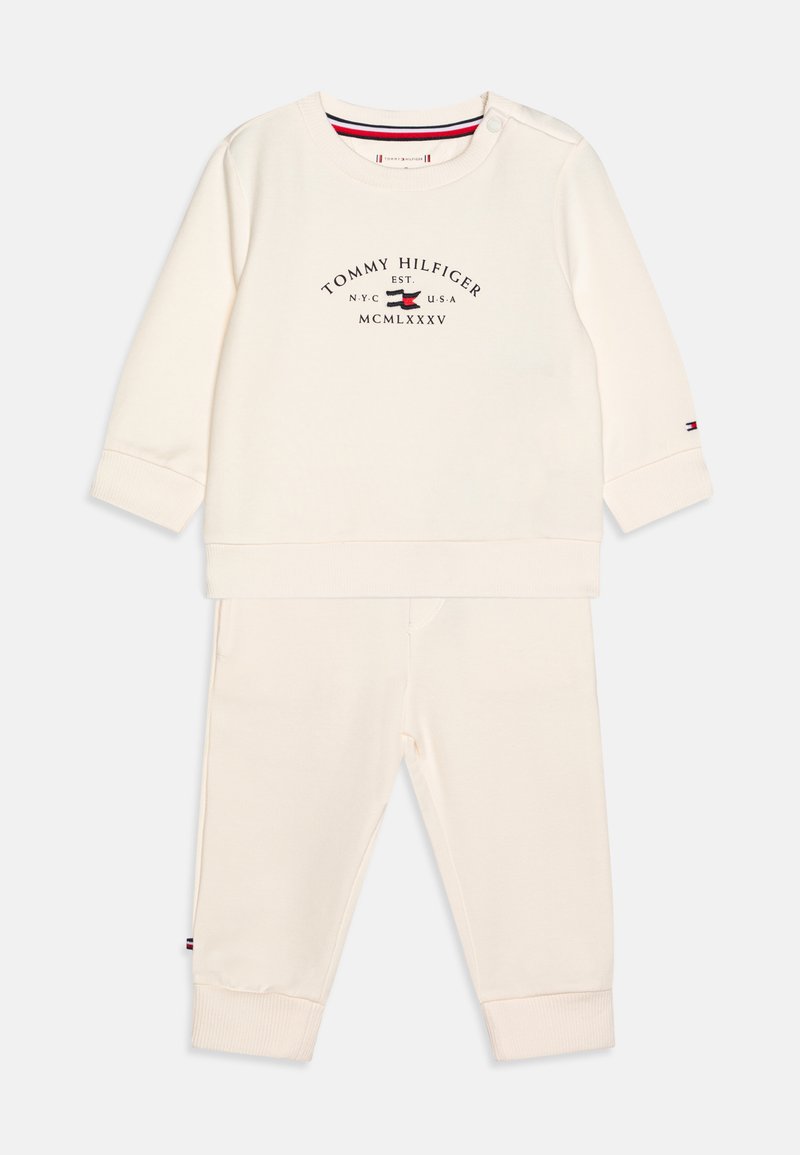 Completo sportivo a due pezzi color crema realizzato in tessuto morbido, composto da un top a maniche lunghe con stampa del logo e pantaloni jogger abbinati con polsini a costine.