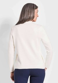 Crème-kleurige trui van zacht tricot materiaal, met lange mouwen, een hoge ronde halslijn en zijsplitten aan de zoom.