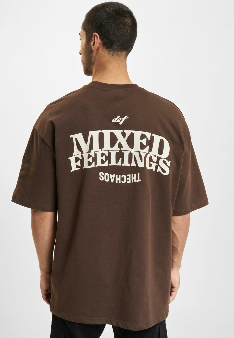 Brun bomull t-skjorte med fet hvit tekst "MIXED FEELINGS" på baksiden, med avslappet passform og kortermede ermer.