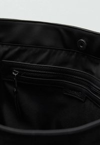 Intérieur d'un sac en tissu noir avec une poche zippée et une fermeture à bouton-pression, doté d'une texture en nylon lisse et d'un logo subtil.