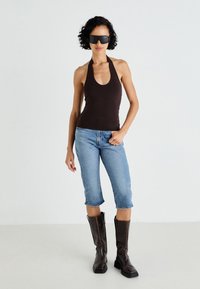 Top halter maro, blugi scurți bleu deschis și cizme din piele maro până la genunchi cu vârf pătrat. Ochelari de soare negri completează ținuta.