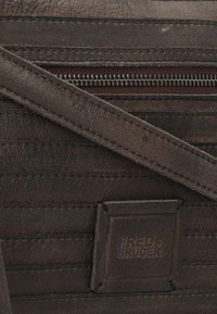 Braune Ledertasche mit strukturierten vertikalen Streifen und einem Reißverschluss. Enthält ein geprägtes Markenpatch mit "FRED's BRUDER." Sichtbare, langlebige Nähte.