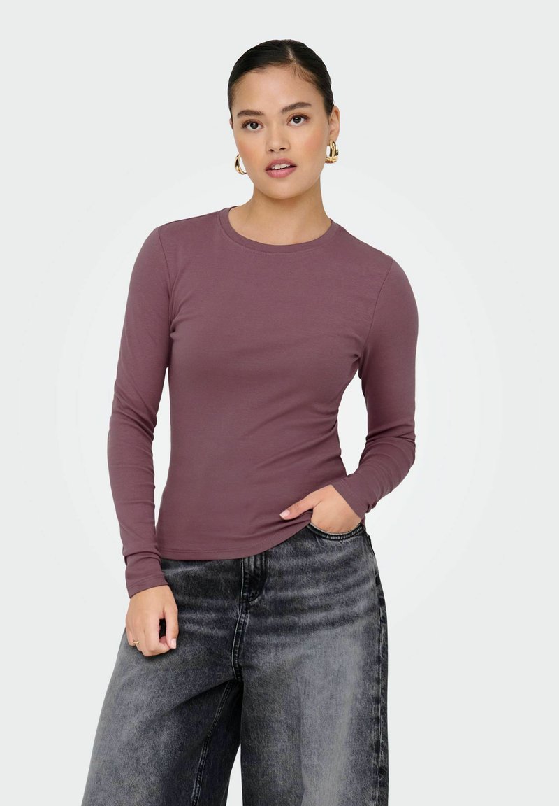 Top a maniche lunghe in tessuto malva con scollo rotondo, abbinato a jeans neri a vita alta e a gamba ampia. Design semplice e aderente.