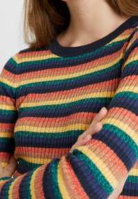 Rippstrickpullover mit horizontalen Streifen in den Farben Rot, Orange, Gelb, Grün und Marineblau; Rundhalsausschnitt und enganliegende Ärmel.
