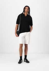 Black knitted polo shirt with short sleeves, paired with white shorts. Black sneakers with white stripes, and a small crossbody bag.