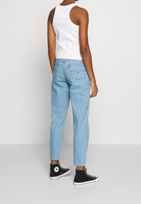 Ljust blå denimjeans med rak passform och klassiska bakfickor. Matchat med en vit ärmlös topp och svarta högstövlar.