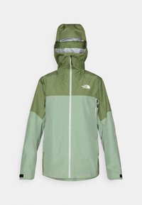 Veste imperméable verte avec capuche, présentant un design bicolore, une fermeture éclair à l'avant et un logo sur le haut de la poitrine gauche. Finition en tissu texturé.