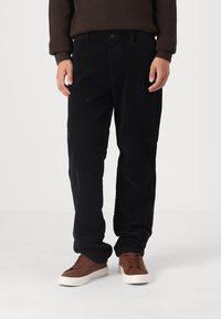Pantaloni din cotele negre, cu o croială dreaptă, care au buzunare frontale și închidere cu nasture, asortați cu adidași de culoare maro deschis.