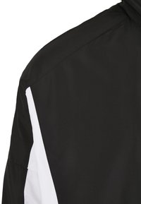 Chaqueta negra con una textura suave y acentos blancos a lo largo de las costuras laterales, que destaca por su diseño elegante y moderno ajuste.