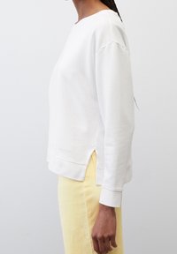 Felpa bianca con colletto a girocollo, spalle scese e spacchi laterali. Realizzata in tessuto morbido, presenta un discreto logo del marchio all'orlo.