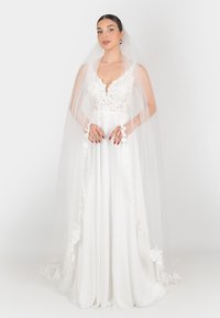 Abito da sposa con corpetto in pizzo e gonna in satin fluida. Presenta dettagli in pizzo floreale e un lungo velo trasparente. Colore: bianco.