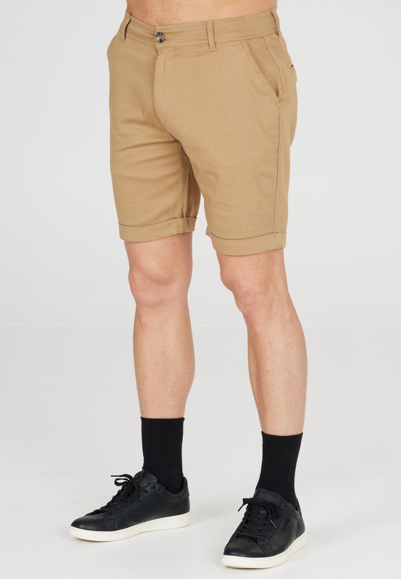 Beige shorts met een aansluitend ontwerp, omgeslagen zoom en voorkruiszakken, gecombineerd met zwarte sneakers en knielange zwarte sokken.