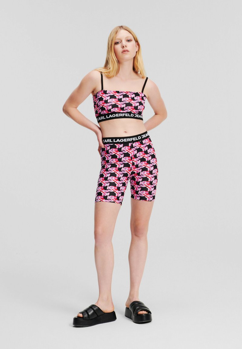 Completo a due pezzi realizzato in tessuto elastico con un motivo geometrico nero, rosa e bianco. Include un top corto e pantaloni coordinati.