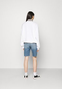 Sudadera blanca de gran tamaño combinada con shorts de mezclilla azul claro, con dobladillos deshilachados. Zapatillas negras con detalles en blanco completan el conjunto.