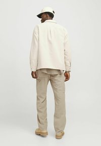 Beige corduroyjas met een ontspannen pasvorm en een rugplooitje, gecombineerd met lichtbeige cargobroeken. Aangevuld met een lichte baseballcap.