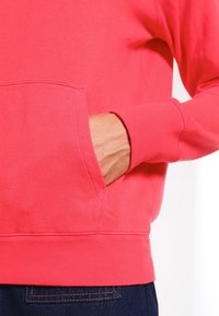 Korálová mikina s kapsou vpředu, žebrovanými manžetami a lemem. Měkká textura látky a volný střih.