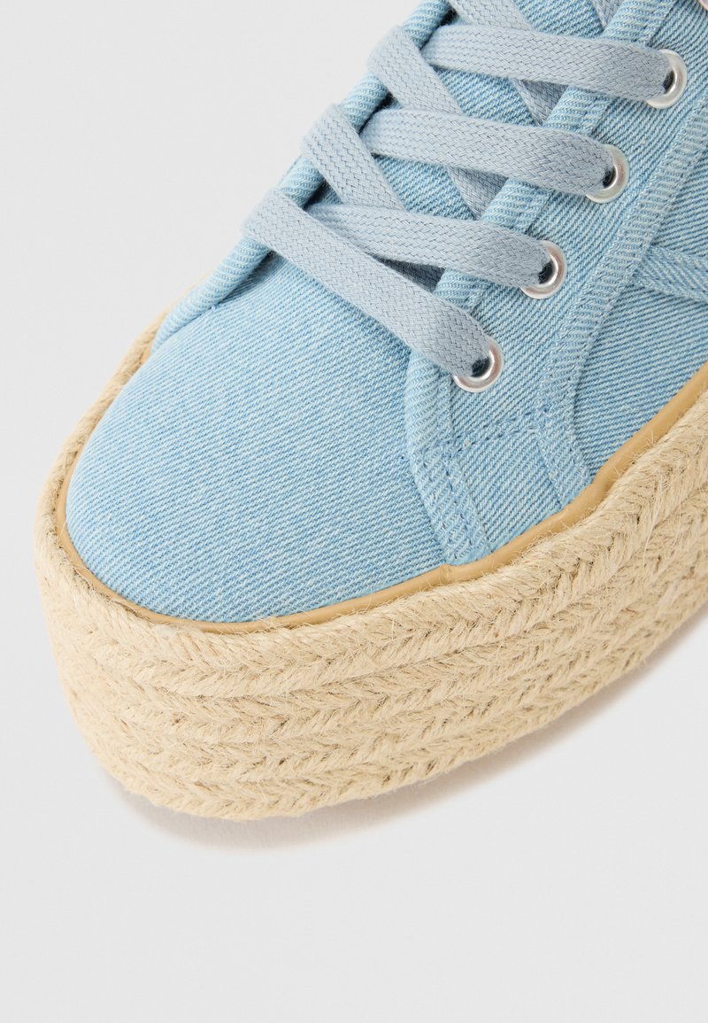 Sneaker platform in denim azzurro con accento in juta intrecciata, dotato di lacci piatti, occhielli e tessuto testurizzato. Design complessivo con punta arrotondata.