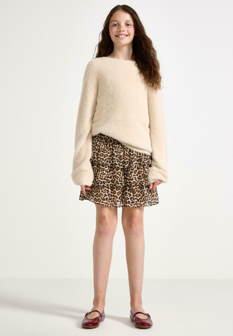 Maglione beige peloso con maniche lunghe, abbinato a una gonna arricciata con stampa leopardata marrone. Scarpe bordeaux completano l'outfit.