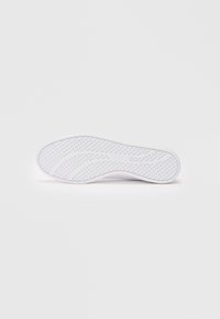 Semelle de basket blanche avec une surface texturée présentant des motifs circulaires et ondulés. Fabriquée en caoutchouc, conçue pour la traction et la stabilité.