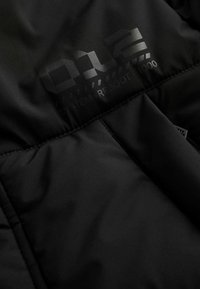 Čierna vypchávkovaná bunda so sekciou obsahujúcou lesklý nápis "012 SYSTEM REBOOT 1000." Hladká tkanina s jemným leskom a prešívanými detailmi.