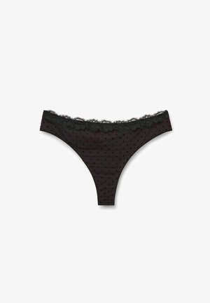Black thong with polka dot pattern, lace trim at the waistband, soft fabric, and a smooth texture. Classic design with delicate detailing.