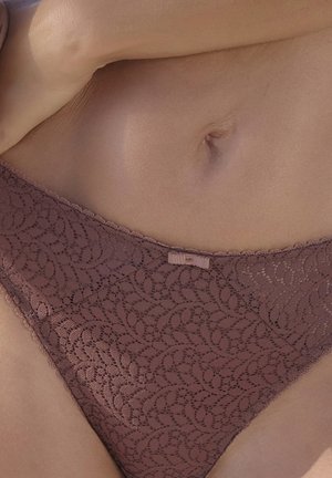 Záber zblízka na dolnú časť brucha osoby, ktorá má na sebe fialkové čipkované spodné prádlo s malou ozdobnou mašličkou v strede pásu.