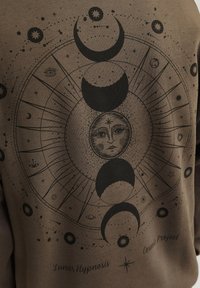 Sudadera marrón con un gráfico de temática lunar en negro. El diseño incluye las fases de la luna, estrellas y símbolos celestiales con texto debajo.
