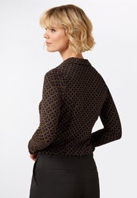 Maglietta a maniche lunghe nera con un motivo geometrico in rosso, giallo e arancione. Tessuto liscio, design aderente, scollatura a girocollo.