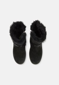 Bottines noires en suède avec doublure en fausse fourrure. Dotées d'un bout arrondi et d'une sangle ajustable autour de la cheville.