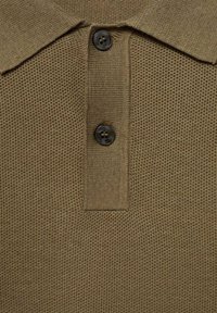 Ruskea teksturoitu polo-paita, jossa on neulemateriaali, klassinen kaulus ja kaksi mustaa nappia edessä kiinnitystä varten.