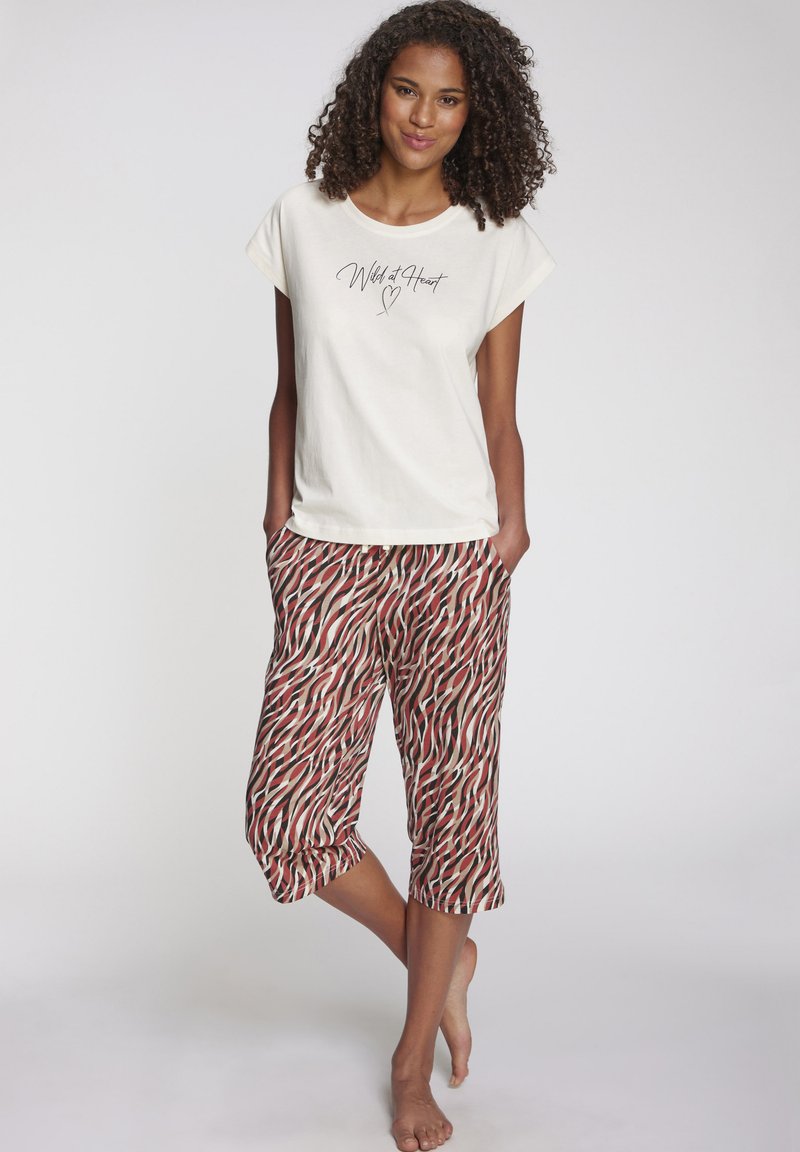 Cremefarbiges Baumwoll-T-Shirt mit dem Aufdruck "Wild at Heart" in Schwarz. Gemusterte, knöchellange Hose mit roten und beigen wellenförmigen Streifen und elastischem Taillenbündchen.