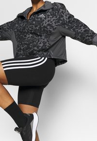 Černá a šedá zipová bunda s leopardím vzorem, elastickými manžetami a logem Adidas. Nosit s černými cyklistickými kraťasy a černými ponožkami s pruhy.