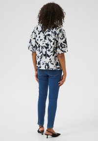 Blusa a maniche corte con un motivo floreale nei colori blu navy, crema e azzurro chiaro; abbinata a jeans blu skinny e mule nere.