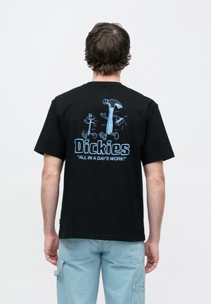 Fekete pamut póló kék grafikával a hátoldalon, amely szerszámokat és a „Dickies” márkanevet tartalmazza a „All in a Day's Work” szlogennel.