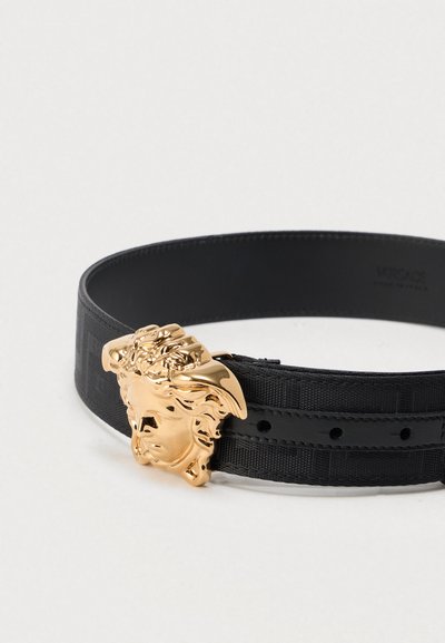 Μαύρη ζώνη με υφασμάτινο σχέδιο και αγκράφα με χρυσή κεφαλή Μέδουσας. Η ζώνη έχει λεία υφή και πολλαπλές τρύπες για ρύθμιση.