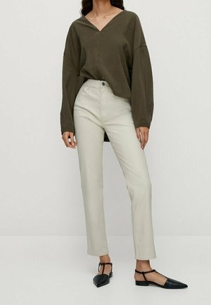 Frau trägt olivgrüne V-Ausschnitt Langarmbluse, hoch taillierte, offwhite gerade geschnittene Hose und schwarze spitze flache Schuhe.