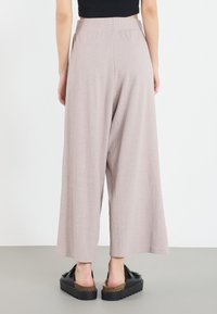 Světle růžové kalhoty s širokými nohavicemi z texturované látky, s vysokým pasem a jemnými svislými pruhy, doplněné černými platformovými botami.