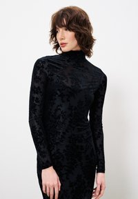 Schwarzes Samtkleid mit hohem Kragen, langen Ärmeln und strukturierten Blumenmustern. Glatte Textur und figurbetonte Silhouette.