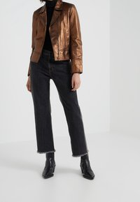 Metalická bronzová kožená motorkářská bunda se zapínáním na zip, zkombinovaná s tmavými džínami s vysokým pasem a černými kotníkovými botami s špičatou špičkou.