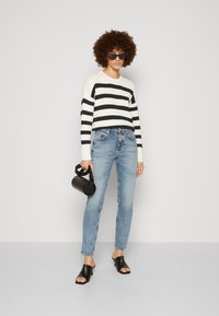 Striped knit sweater in cream and navy, light blue denim jeans, black open-toe mules, and a round black handbag. Smooth textures, casual fit.